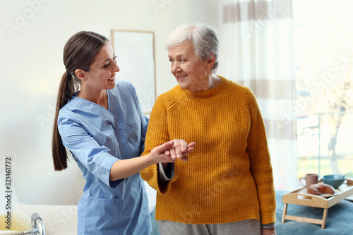 Care worker helping elderly woman to walk in geriatric hospice