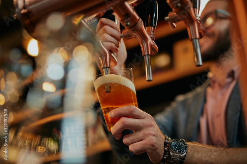 Tattooed caucasian barman pouring beer while standing in pub.