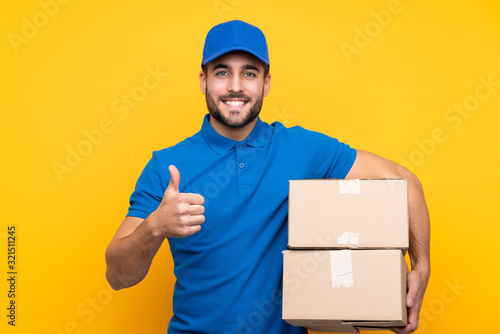 Delivery man over isolated yellow background with thumbs up because something good has happened