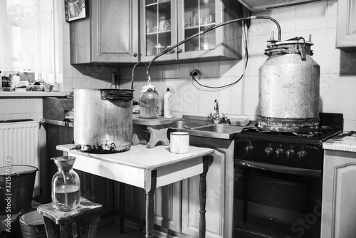 Old-fashioned moonshine machine for creating homemade strong alcohol in the kitchen. Process of distillation, general view. Story about an aged way of distilling moonshine at home. Monochrome effect