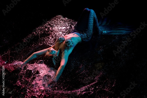 Mermaid splashing in water under pink light