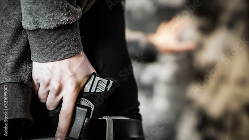 Man holding out hand while drawing a concealed pistol. Personal protection concept