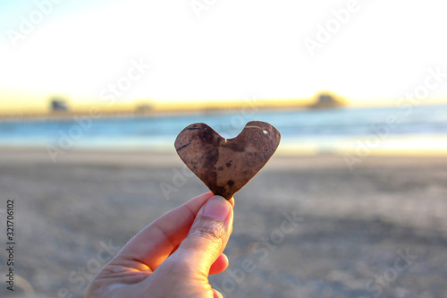 Hand holding heart in front of the ocean and pier in Oceanside California