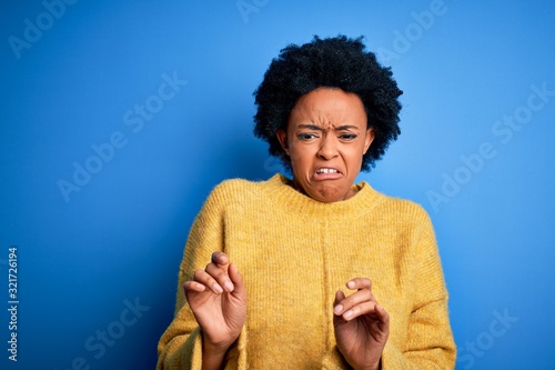 Young beautiful African American afro woman with curly hair wearing yellow casual sweater disgusted expression, displeased and fearful doing disgust face because aversion reaction.