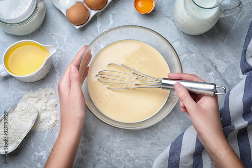 Woman preparing batter for thin pancakes at grey table, top view