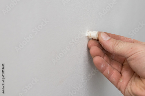 male hand pokes a plastic dowel into a white drywall wall