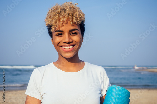 Young brazilian woman wearing casual cotton white t-shirt and holding yoga mat on beach
