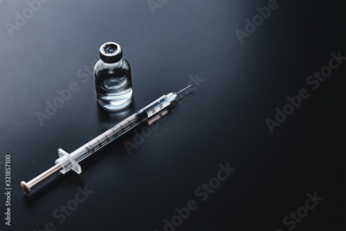 Medical syringe and ampoule with medicine on the black background, top view with copy space. Vaccination and virus protection concept