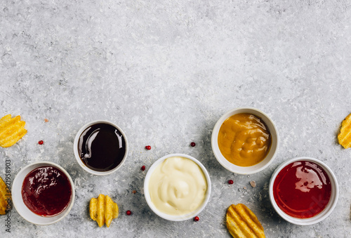 White bowls of various dip sauces on gray background. Mustard, ketchup, cheese, teriyaki and cranberries sauces. Top view with copy space. Flat lay