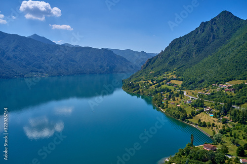 Panoramic view of the mountains and Lake Idro. Reflection in the water of the mountains, trees, blue sky. Aerial view, drone photo