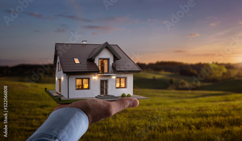 Concept of buying or building new home. Male hand showing, offering a new dream house at the empty field with copy space