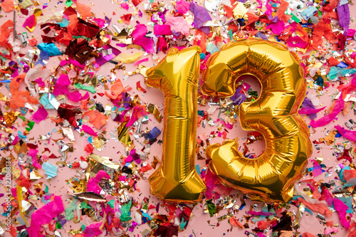 Number 13 gold birthday celebration balloon on a confetti glitter background