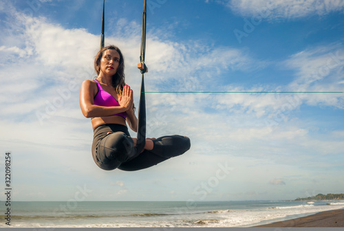 aero yoga beach workout - young attractive and athletic woman practicing aerial yoga meditation exercise over the sea training acrobatic body postures isolated on blue sky