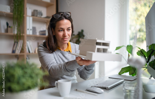 Architect with model of a house sitting at the desk indoors in office.