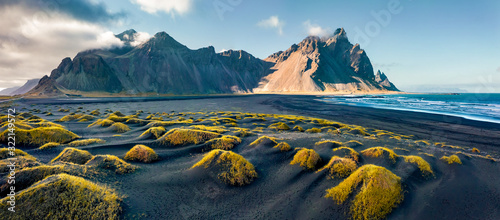 View from flying drone. Stunning autumn scene of Stokksnes cape with Vestrahorn (Batman Mountain) on background. Panoramic Icelandic view of black sand dunes with fresh green grass.