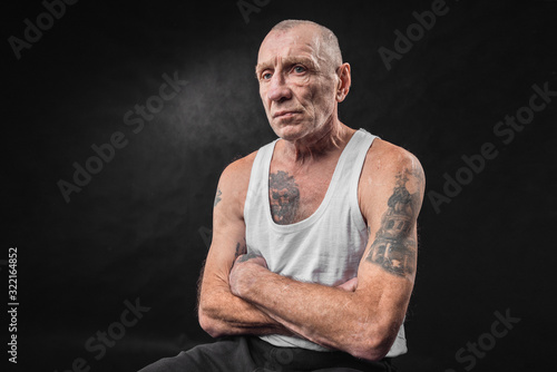 Portrait of an old man with tattoos in a white T-shirt on a black background