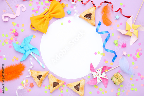 Purim holiday composition. Cookies with party supplies on purple background