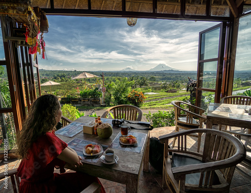 Young brunette girl having breakfast with view over the Jatiluwih rice terrace from open restaurant on Bali, Indonesia 