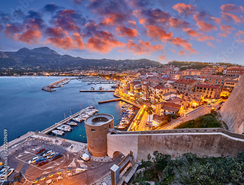 View from the walls of the citadel of Calvi on the old town with historic buildings at evening sunset. Bay with yachts and boats. Luxurious marina and popular tourist destination. Corsica, France