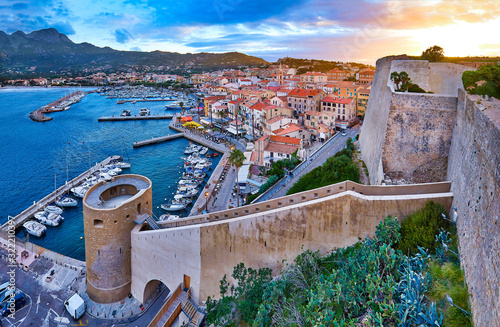 View from the walls of the citadel of Calvi on the old town with historic buildings at evening sunset. Bay with yachts and boats. Luxurious marina popular tourist destination. Corsica, France.