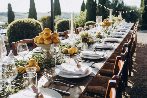 in the back yard of the old villa there is a long festive table, which is decorated with lemons and herbs, on the table are plates, glasses and candles. Wedding in Italy. Tuscany