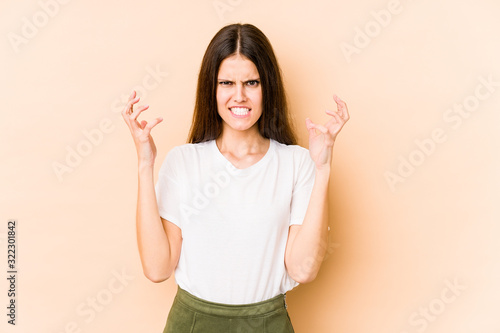 Young caucasian woman isolated on beige background screaming with rage.