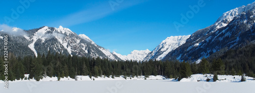 Beautiful snow covered lake in evergreen forested area of the Cascade mountains in Washington State on a gorgeous blue sky day.