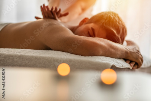 Sports massage. Massage therapist massaging shoulders of a male athlete, working with Trapezius muscle. Toned image. Masseur doing massage on man body in the spa salon. Beauty treatment concept.