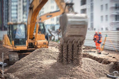 Yellow heavy excavator excavating sand and working during road works, unloading sand during construction of the new road