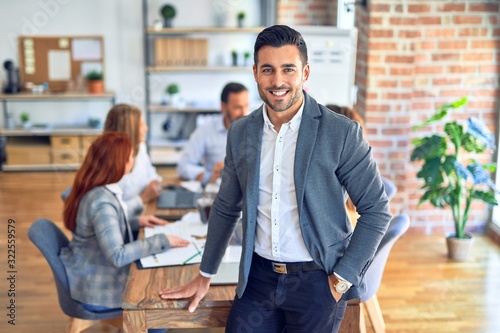 Group of business workers working together. Young handsome businessman standing smiling happy looking at the camera at the office