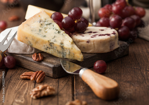Selection of various cheese on the board and grapes on wooden background. Blue Stilton, Red Leicester and Brie Cheese and nuts.