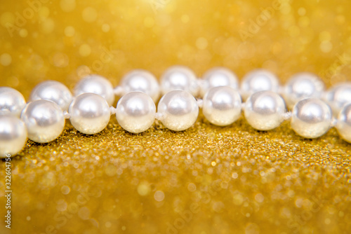 A necklace of pearls lies on a shiny gold background.