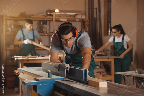 Professional carpenter working with surface planer and colleagues in workshop