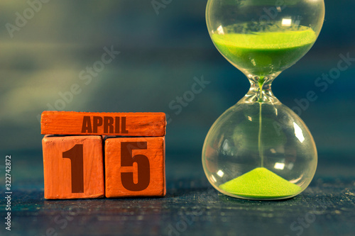 april 15th. Day 15 of month,Handmade wood cube with date month and day and hourglass with green sand. Time passing away. artistic coloring. spring month, day of the year concept