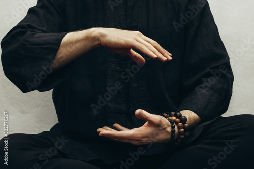 A man in black shirt sitting and doing qigong. Hands direct energy. Prayer, gratitude.Practicing monk. Qi energy. Yoga pose. Close up