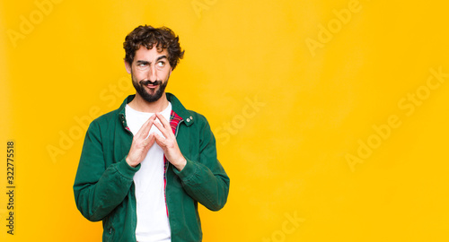 young crazy bearded man scheming and conspiring, thinking devious tricks and cheats, cunning and betraying against flat wall