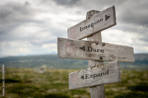 Imagine, dare and expand text on wooden road sign outdoors in nature.