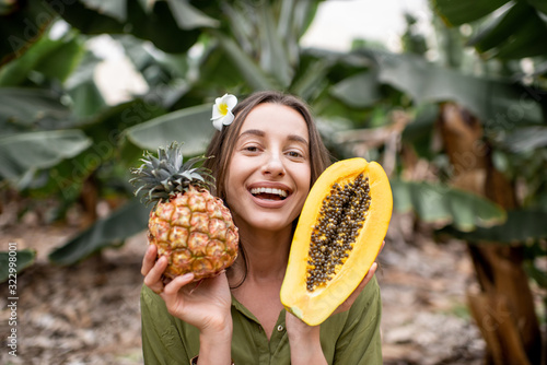 Portrait of a young smiling woman with sliced papaya and ananas outdoors on the tropical plantation. Concept of vegetarianism, healthy eating of fresh fruits and wellbeing