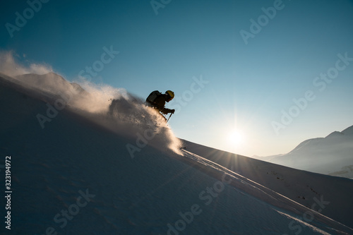 Silhouette of man skier rides down from the snowy hill top