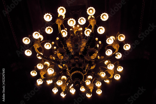 Antigua araña estilo europeo neoclásico iluminada con todas sus luces encendidas sobre fondo negro.