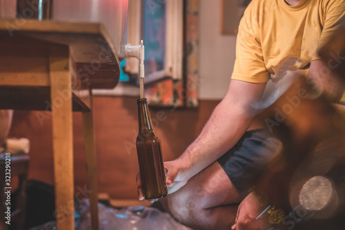 Home craft beer brewery. Final step of pouring a fresh IPA beer into a bottle from fermenter. Hand holding a bottle with home made pale ale beer.