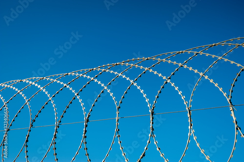 Razor wire fence curving in loops against bright blue sky