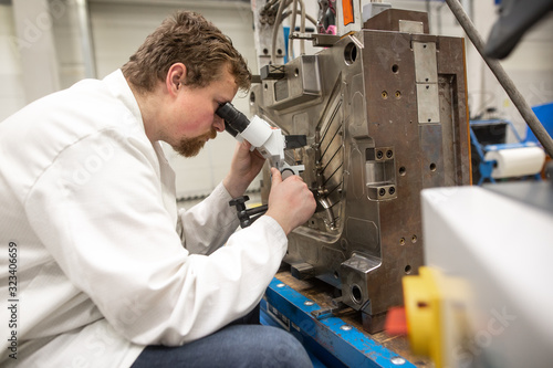 Quality engineer checks deficiencies on the injection mold by a microscope, industrial concept