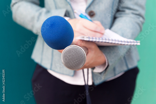 News reporter or TV journalist at press conference, holding microphone and writing notes