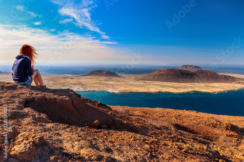 A woman looking at the sea and the island. Location: Europe, Spain, Canary Islands, Lanzarote (near Mirador del Rio; La Graciosa island in the background)
