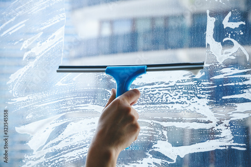 young female hand cleaning dirty glass window with a squeegee