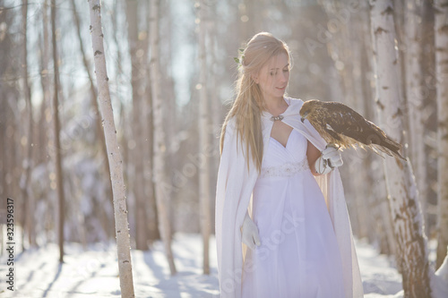 A beautiful girl in a white coat walks in the forest. The huntress with a bird in her hands.