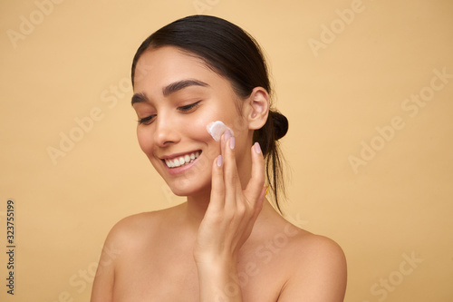 Young girl smiles and puts cream on her face on a yellow background