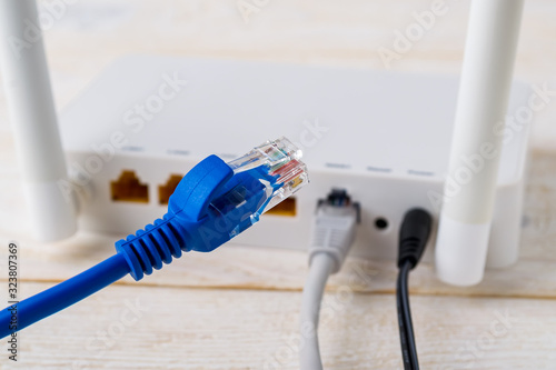 Close-up of blue network cable on a background of a white Wi-Fi wireless router on a white wooden table. Wlan router with internet cables plugged in on a table in a home or office.