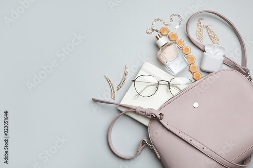 Stylish woman's bag with accessories on light grey background, flat lay. Space for text